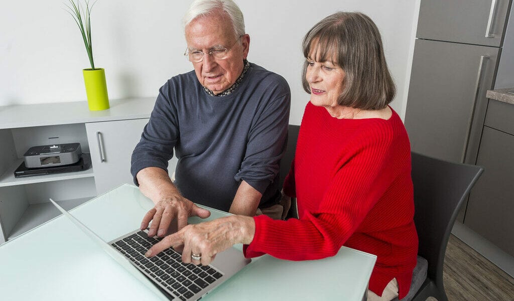 An elderly man and woman point at a laptop as they shop online at home, demonstrating the importance of age inclusive digital marketing