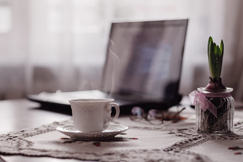 Image of a laptop resting on a table beside a cup of tea and a plant in an elderly persons home. This highlights the need for age inclusive digital marketing during COVID-19