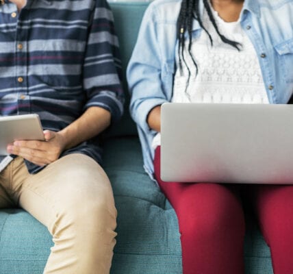 Man and woman sitting side by side using electronic devices