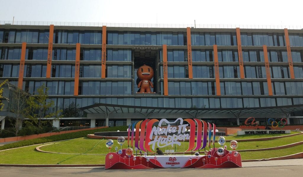 Image of Alibaba's campus in Beijing. A glass building with the mascot in the middle and a slogan 'make it happen' at the forefront of the image.