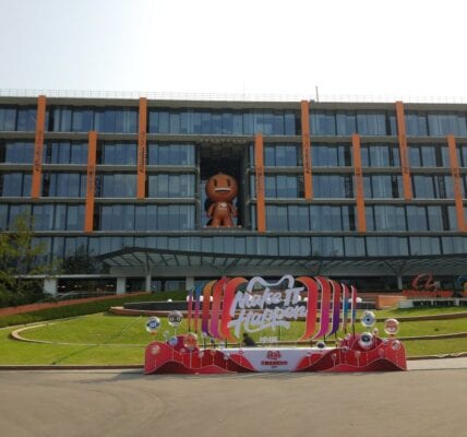 Image of Alibaba's campus in Beijing. A glass building with the mascot in the middle and a slogan 'make it happen' at the forefront of the image.