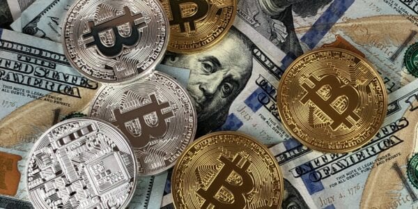 Bitcoin Cryptocurrency coins scattered across some US dollar Hundred dollar bills