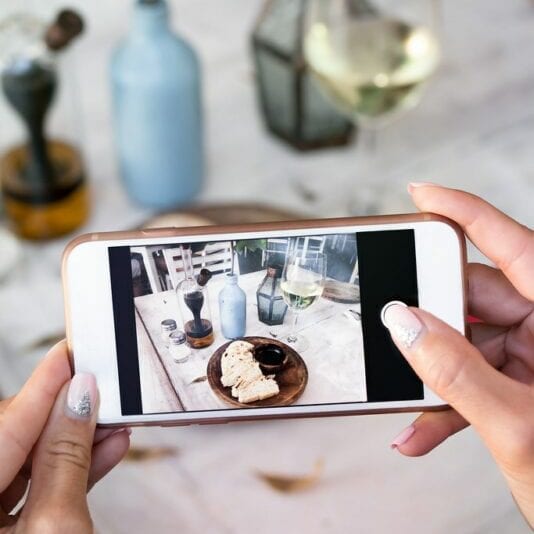 This is an image of a woman using her phone to take a photo of a meal in a restaurant. 