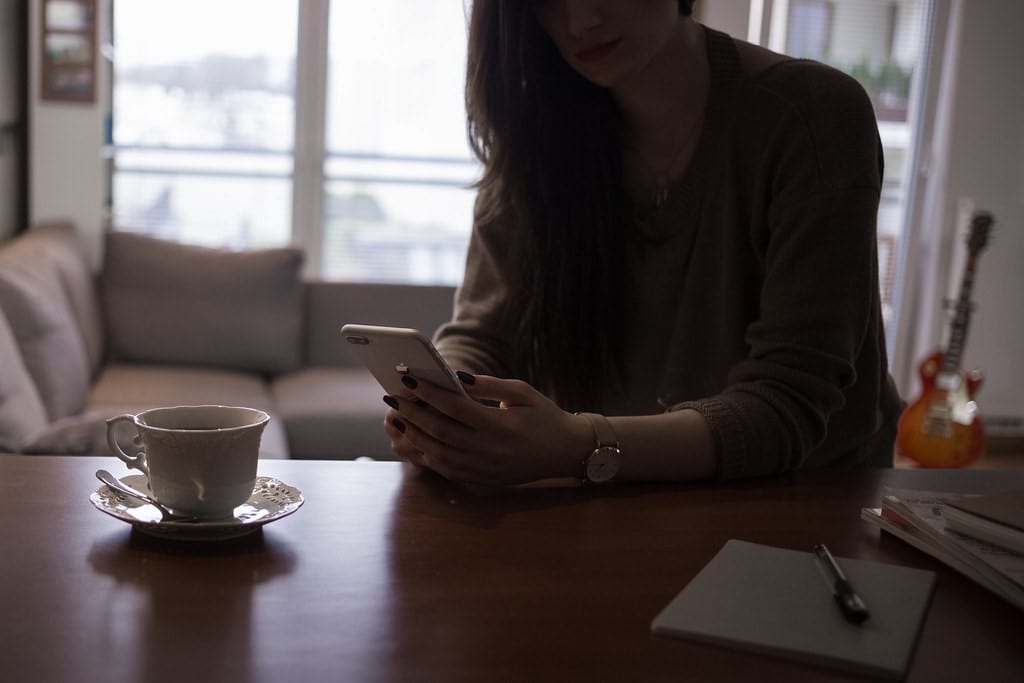 Woman holding a phone and looking at it while drinking coffee. The woman is consuming content which is where short-form video could be used 
