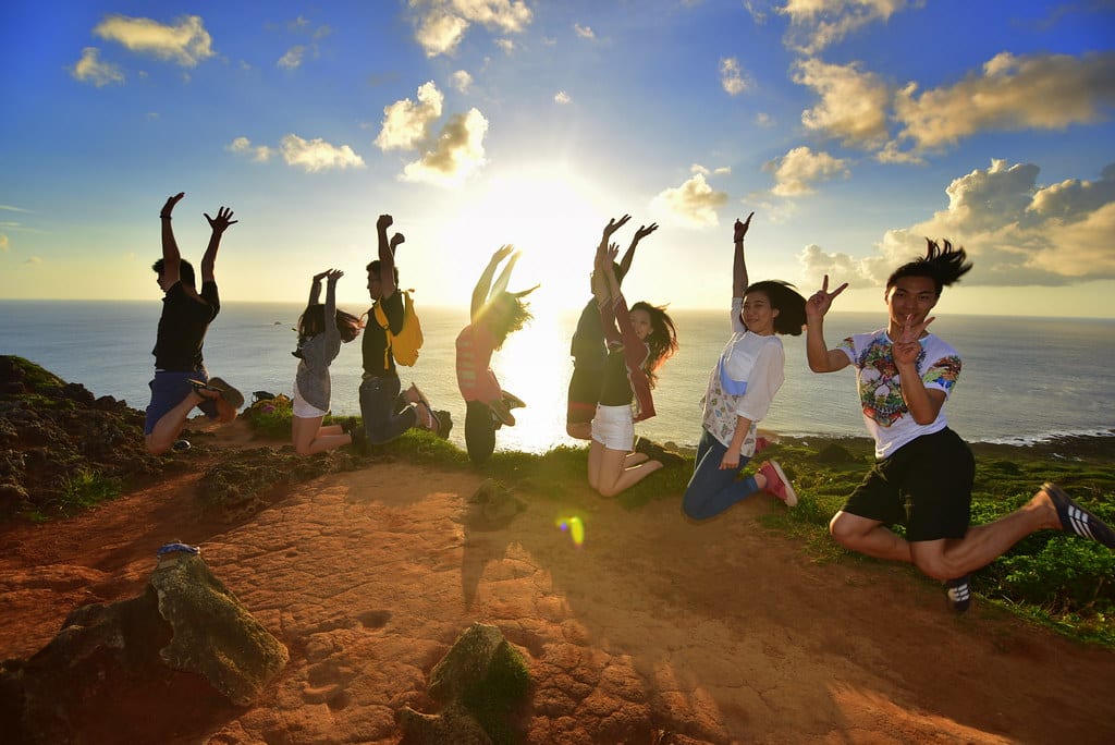 A group jumping in celebration after winning the Instagram competition on a cliff while the sun sets over the sea. 