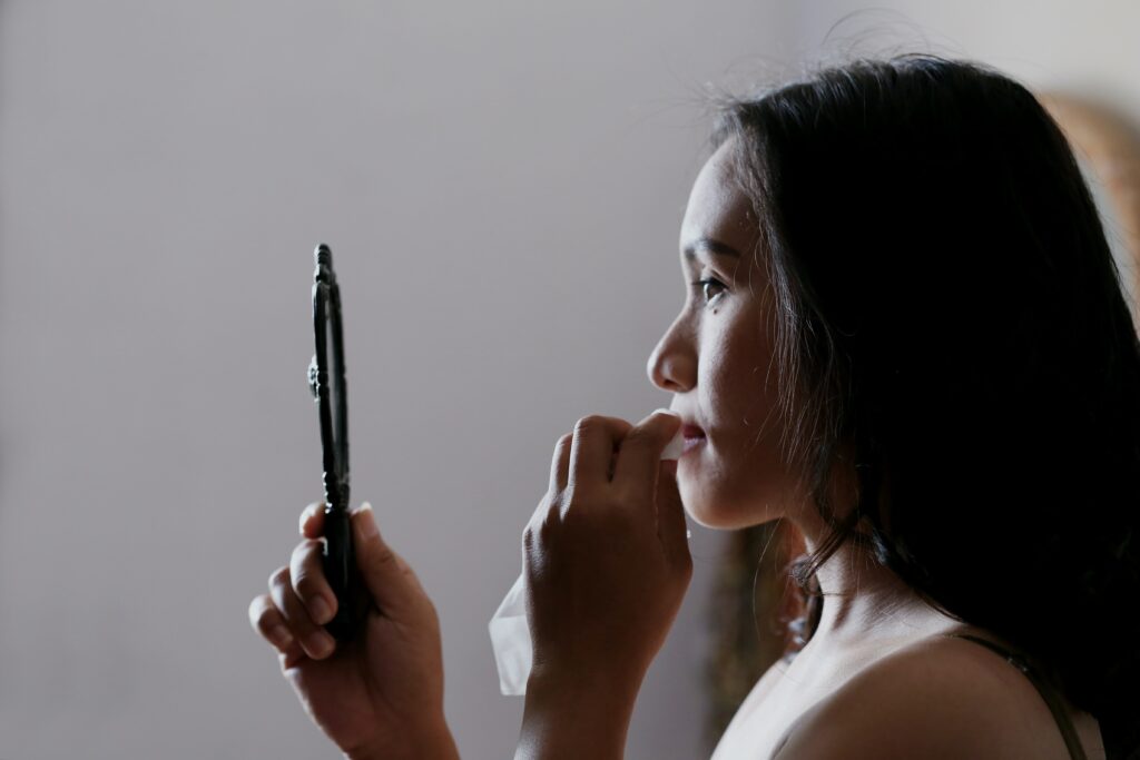 Side profile of woman looking at herself in a handheld mirror removing lipstick