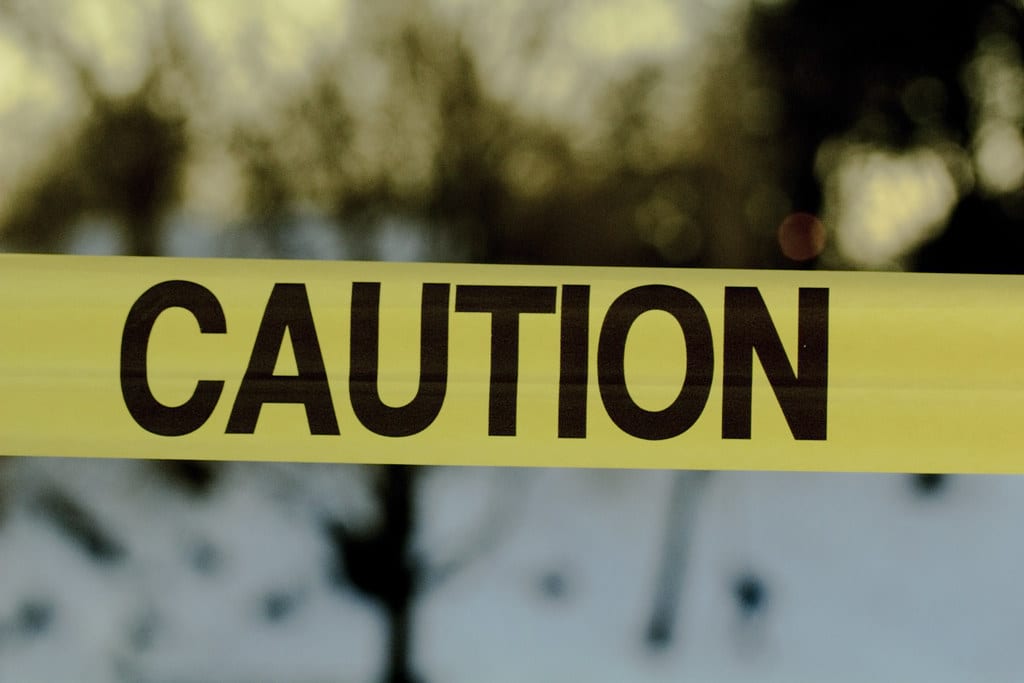 Image of yellow tape with 'caution' written in black bold font with a blurry background of trees and the sun shining indicating the importance of caution in influencer marketing.