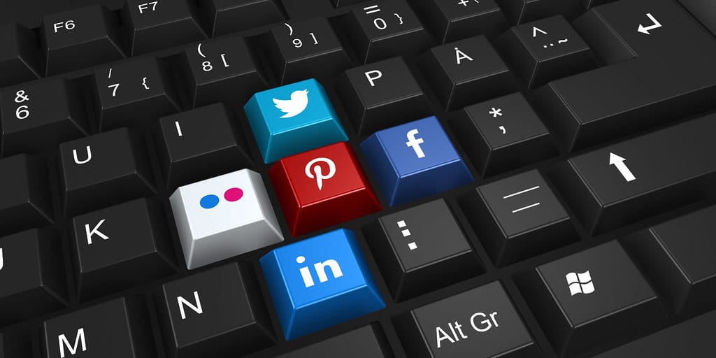 Image of a black and white computer QWERTY keyboard. It shows five keys with the Twitter light blue logo, Facebook dark blue logo, Linkedin pastel blue logo and Flickr white with blue and pink circles logos with the red Pinterest logo in the middle instead of letters. This image shows the 'keys' to success for influencer marketing.