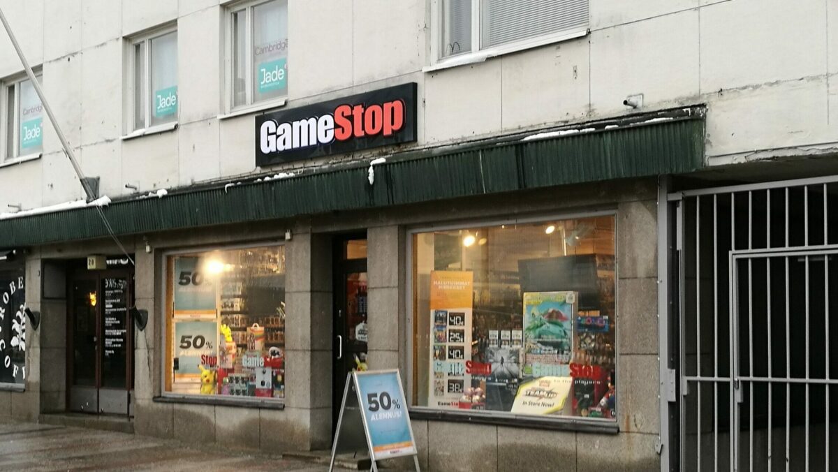 Image of a rundown GameStop store during a clearance sale offering 50% of all products before it's stock market rise. the store is located in a row of shops on an empty street at the bottom of a concrete housing block.