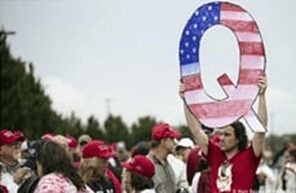 A QAnon supporter at a rally, holding a large 'Q' painted in the colours of the American flag. 
