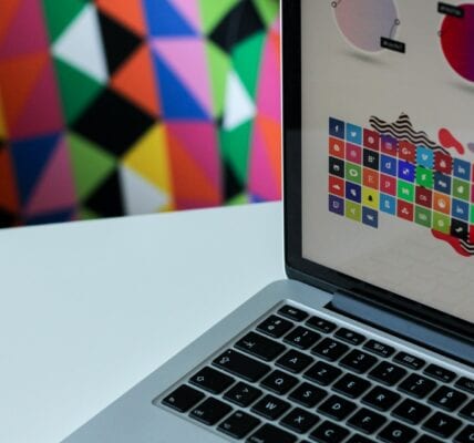 Laptop displaying a graphic design website. Behind the laptop is a colourful wall