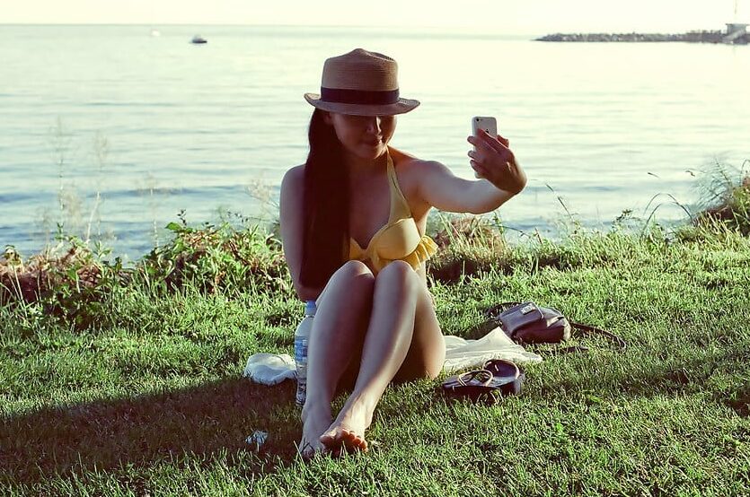 Image of influencer taking a selfie for at a lake on a sunny day.