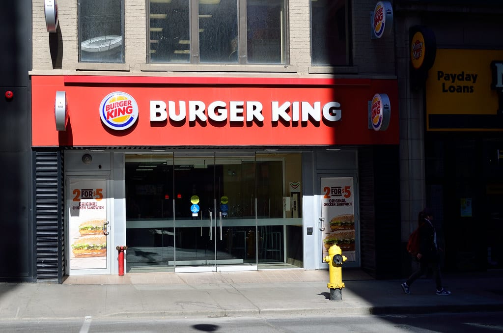 Image of a closed Burger King in the city. There is still sun shining on the building, but a shadow is starting to creep over it from the right.