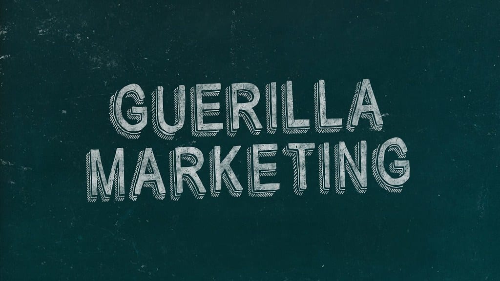 Image of a green chalkboard with "GUERILLA MARKETING" written on it with white chalk and in 3D writing.