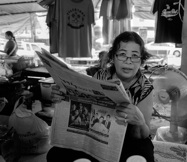 Image of a lady reading a newspaper with a lot of advertisements, a form of traditional marketing.