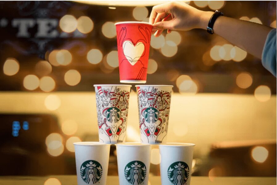 6 Starbucks coffee cups stacked in a pyramid with doodles and drawings on the top 3.