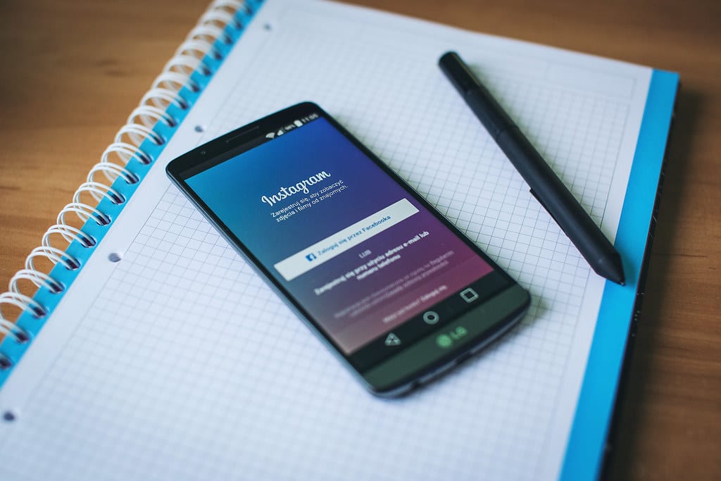 A phone on a desk on top of a notebook. The Instagram log-in page is open on the phone. There is a pen located to the right of the phone. 