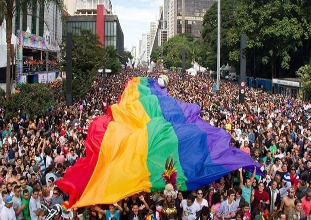 An LGBTQ+ Pride Flag suspended by a crowd during a parade.