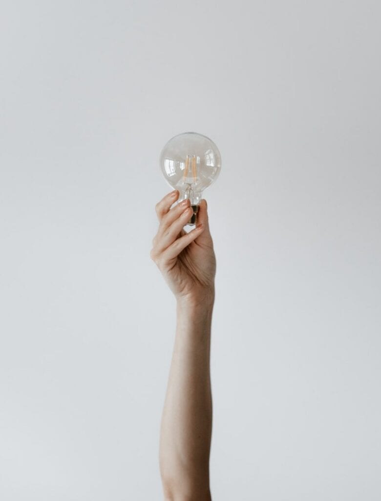 Picture of a person's arm holding a switched off lightbulb in their hand.