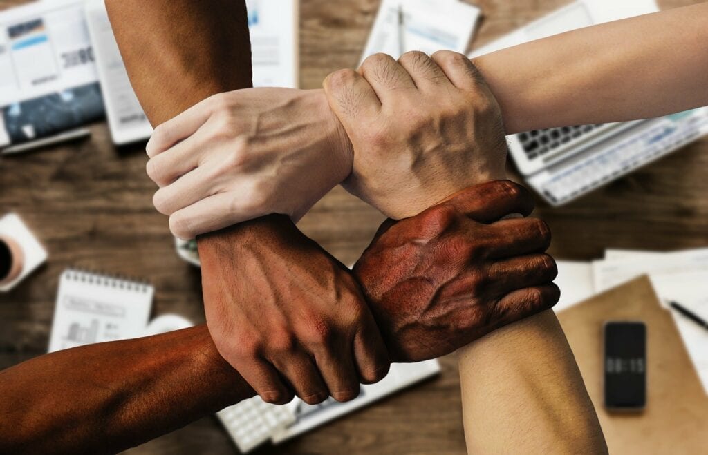 Four people with different skin colours holding each others wrists in unity above a work desk